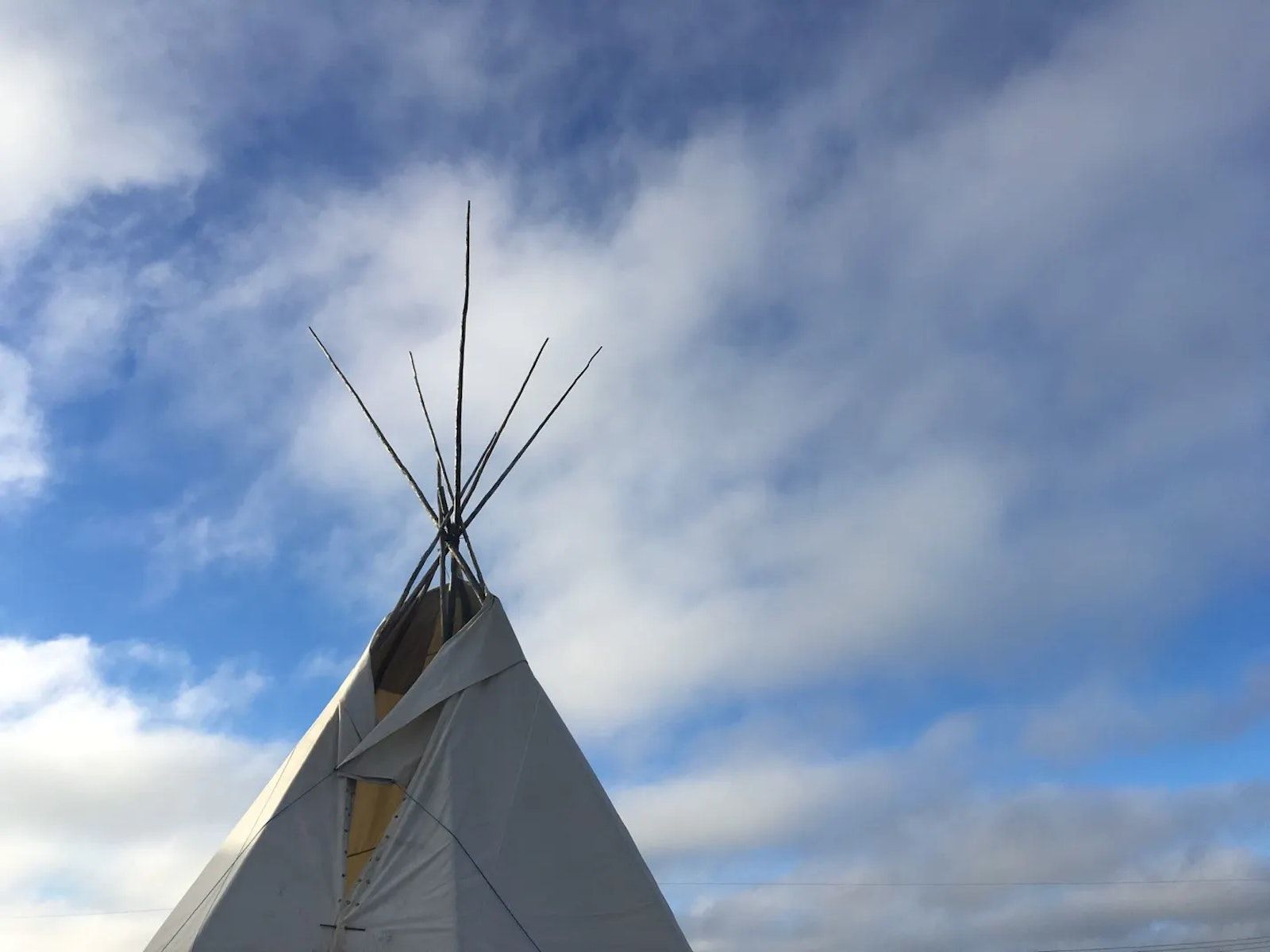 Top of a teepee with clouds and blue sky in the background