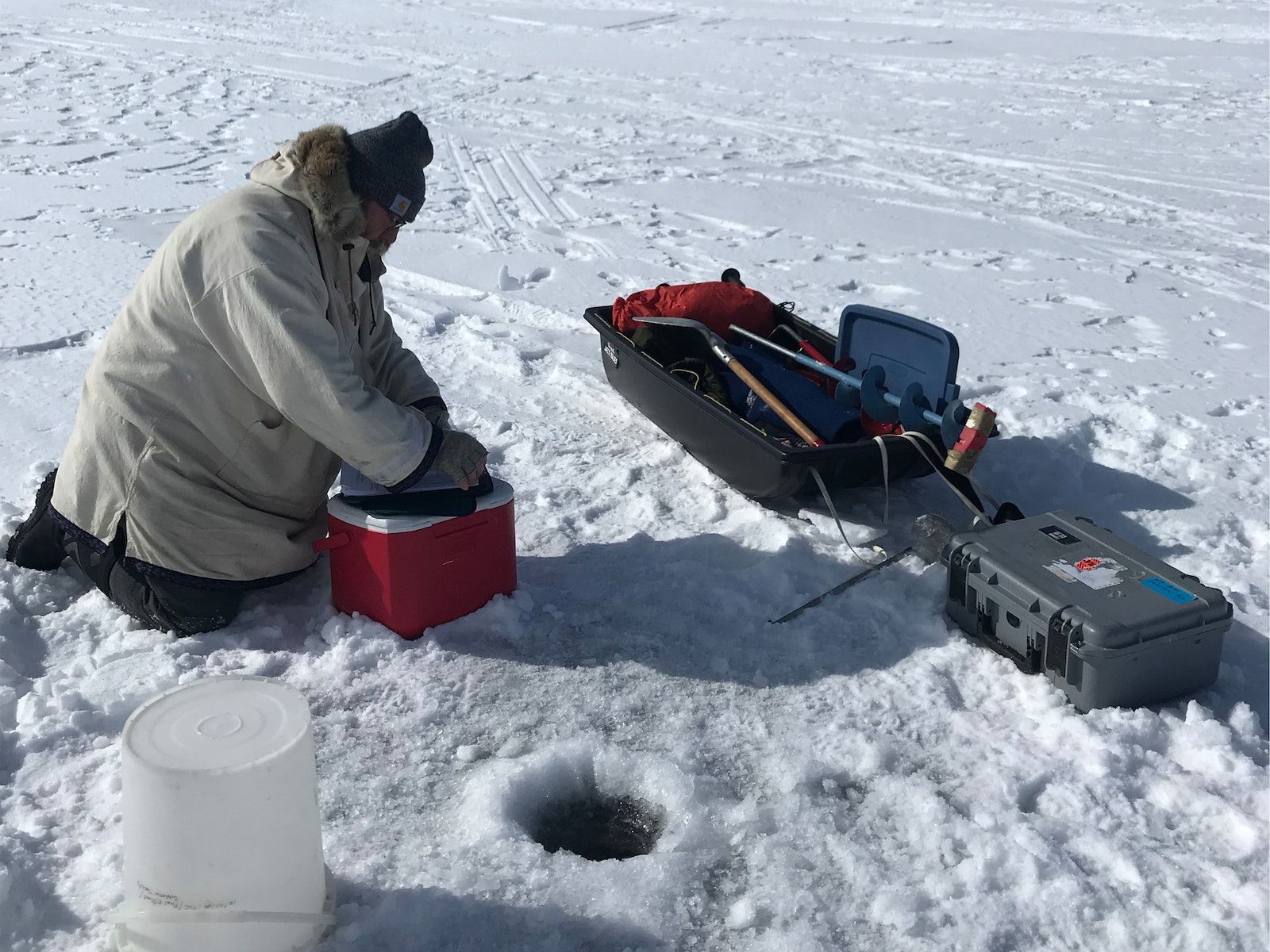 Bénévole LakeKeepers à genoux sur le lac Chestermere gelé avec équipement de surveillance de l'eau en hiver