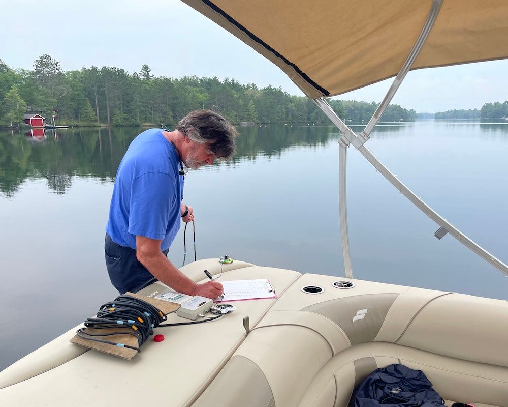A man is recording measurements being taken off of a boat on the lake