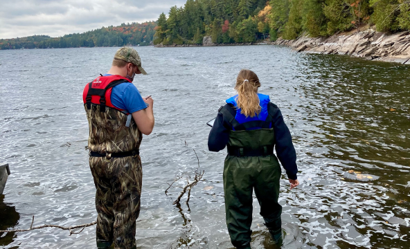 Deux chercheurs debout dans un lac mesurant la qualité de l’eau avec un équipement portable.
