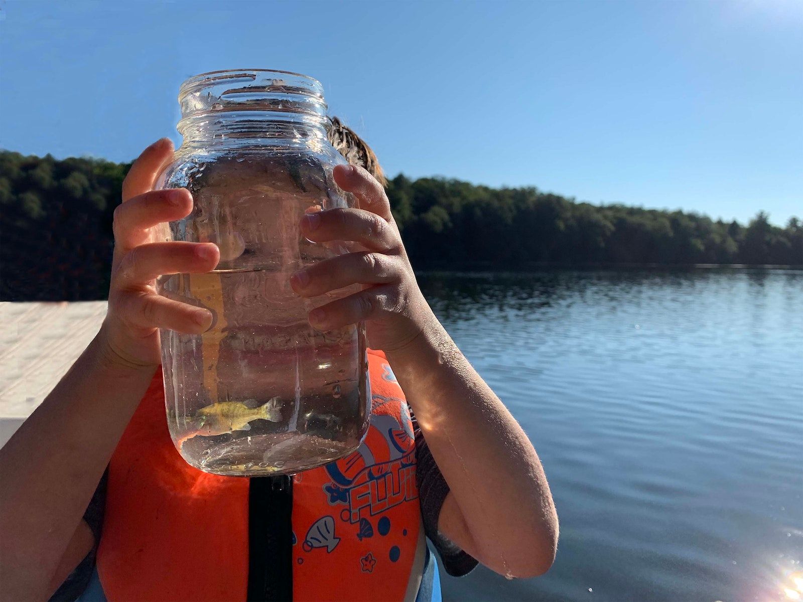 A child holding glass jar housing a fish